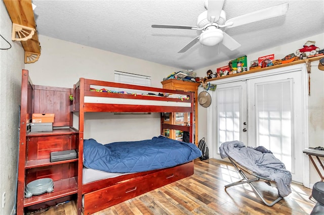 bedroom with a textured ceiling, ceiling fan, hardwood / wood-style flooring, and french doors