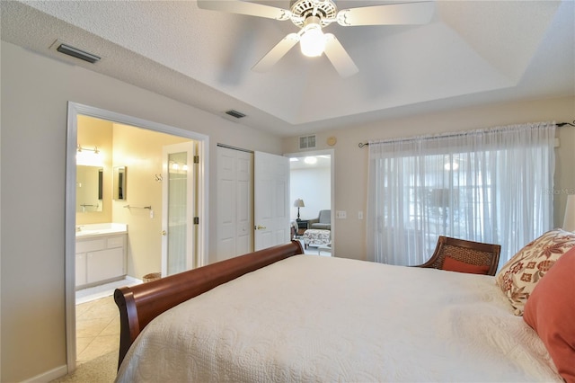 tiled bedroom featuring a closet, ensuite bath, a tray ceiling, and ceiling fan