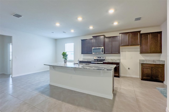 kitchen featuring light stone counters, stainless steel appliances, a kitchen island with sink, and light tile flooring