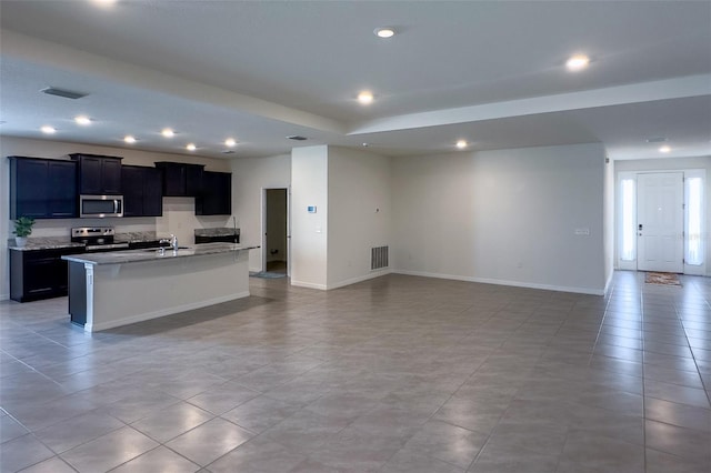 kitchen with a kitchen island with sink, stainless steel appliances, sink, and light tile flooring