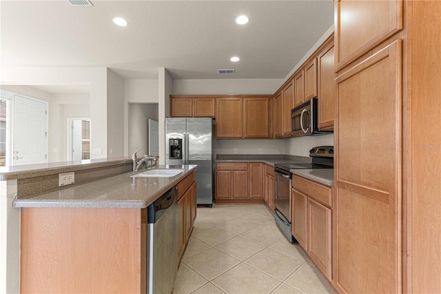 kitchen with light tile patterned flooring, light stone countertops, appliances with stainless steel finishes, sink, and a center island with sink