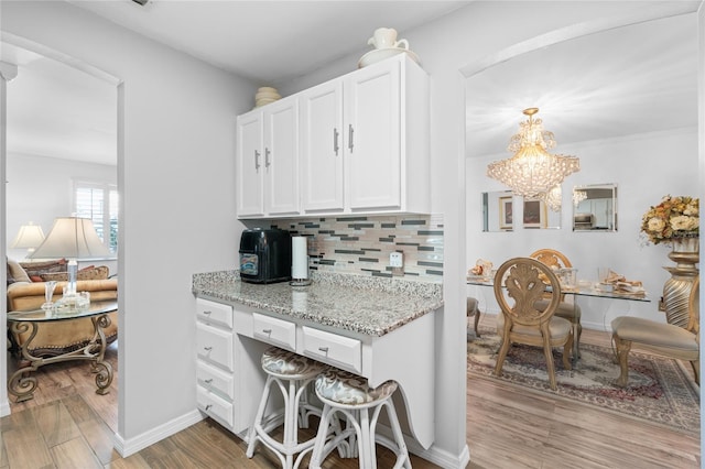 kitchen featuring tasteful backsplash, light stone counters, white cabinets, an inviting chandelier, and light wood-type flooring