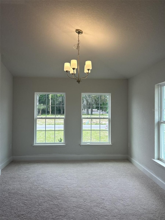 carpeted empty room with a healthy amount of sunlight and an inviting chandelier