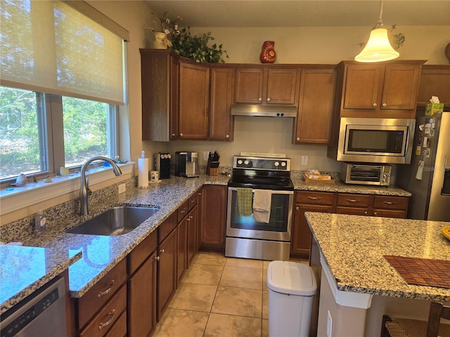 kitchen featuring appliances with stainless steel finishes, decorative light fixtures, light stone counters, and sink