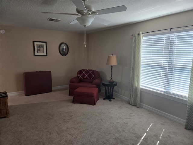 living area with a textured ceiling, light colored carpet, and ceiling fan