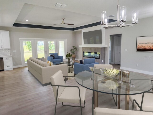 living room featuring light wood-type flooring, french doors, ceiling fan with notable chandelier, a tile fireplace, and a tray ceiling