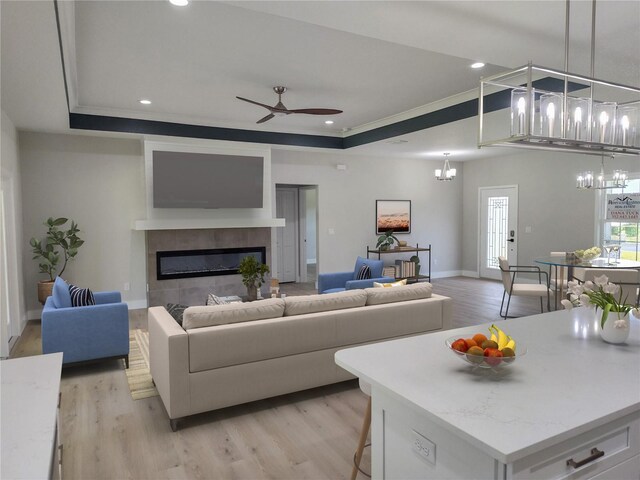 living room with ceiling fan with notable chandelier, a raised ceiling, and light hardwood / wood-style floors