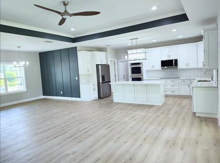 kitchen with ceiling fan with notable chandelier, stainless steel appliances, white cabinetry, a center island, and light hardwood / wood-style flooring