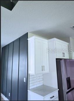 interior space featuring decorative backsplash, white cabinetry, and stainless steel fridge with ice dispenser