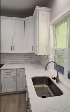 kitchen with hardwood / wood-style floors, sink, tasteful backsplash, and white cabinetry