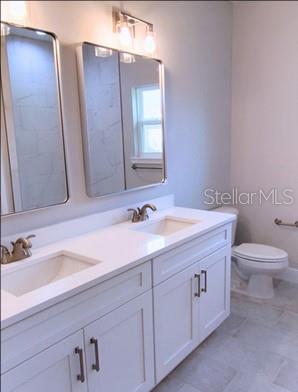 bathroom featuring toilet, dual bowl vanity, and tile patterned floors