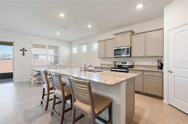 kitchen with sink, an island with sink, light tile floors, stainless steel appliances, and a breakfast bar area