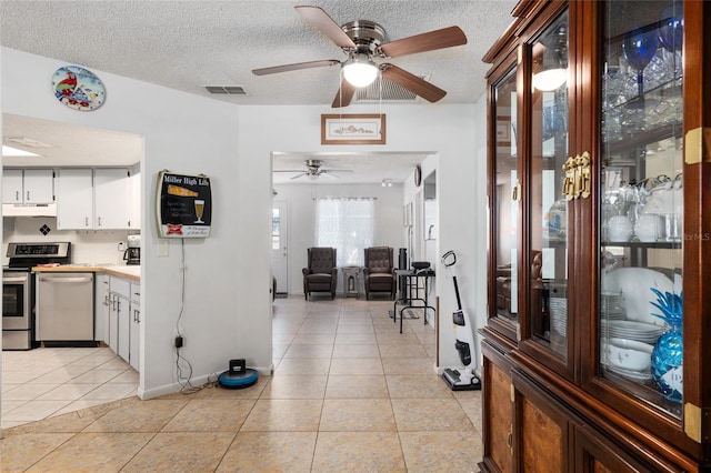 kitchen with stainless steel dishwasher, ceiling fan, light tile floors, and white cabinetry