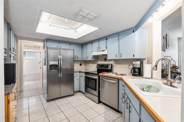 kitchen featuring light tile floors, a textured ceiling, and stainless steel appliances