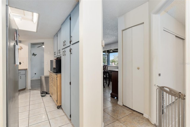 corridor featuring a skylight, a textured ceiling, and light tile flooring