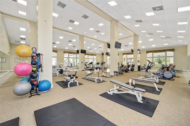 exercise room with a paneled ceiling, light carpet, and a high ceiling