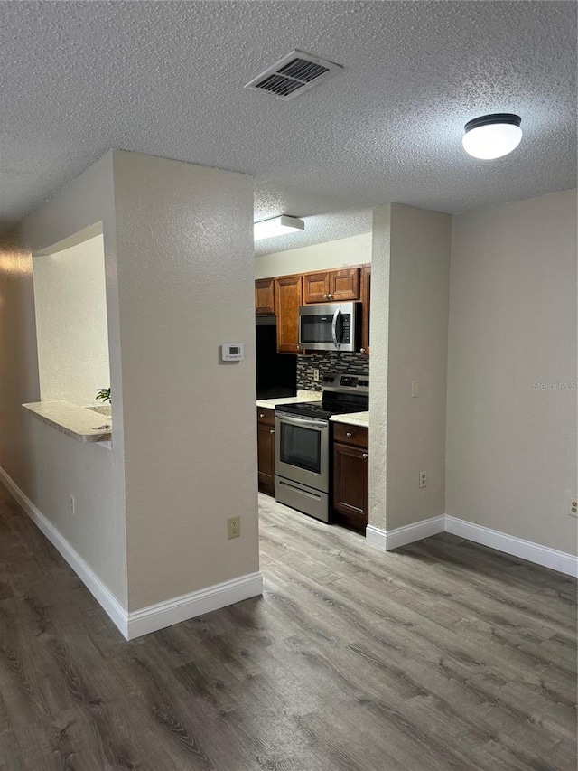 kitchen featuring decorative backsplash, appliances with stainless steel finishes, a textured ceiling, and hardwood / wood-style flooring