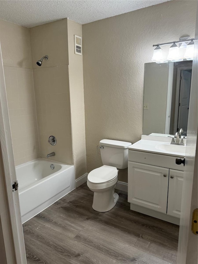 full bathroom with a textured ceiling, hardwood / wood-style flooring, toilet, and tiled shower / bath