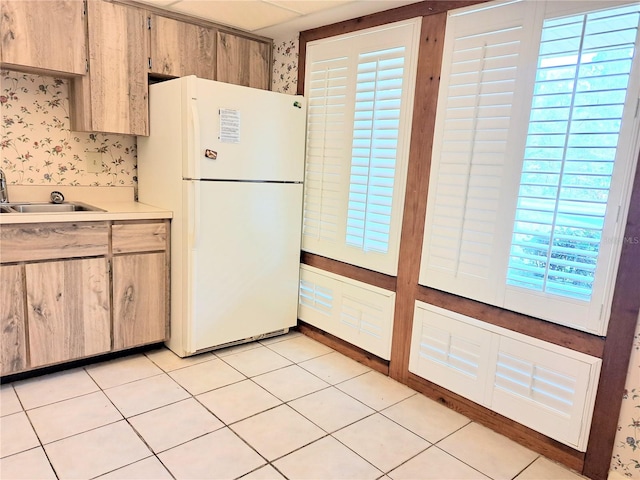 kitchen featuring light brown cabinets, sink, light tile patterned floors, a wealth of natural light, and white fridge