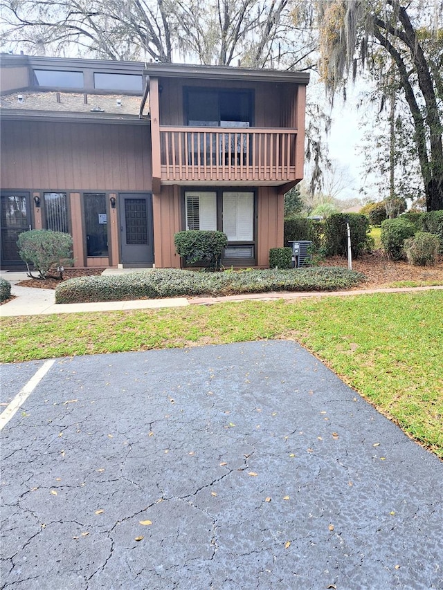 view of front of property featuring a front yard, a balcony, and central AC