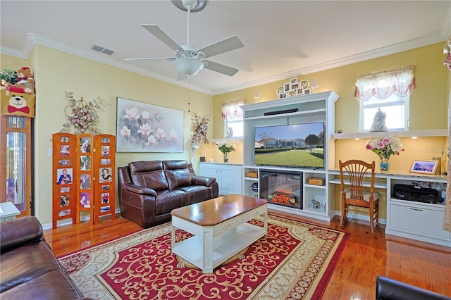 living room featuring visible vents, a ceiling fan, ornamental molding, wood finished floors, and a fireplace