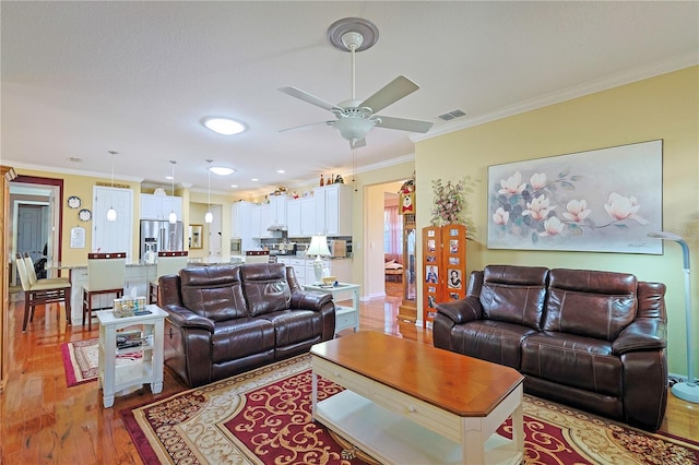 living area with light wood-style floors, ceiling fan, visible vents, and crown molding