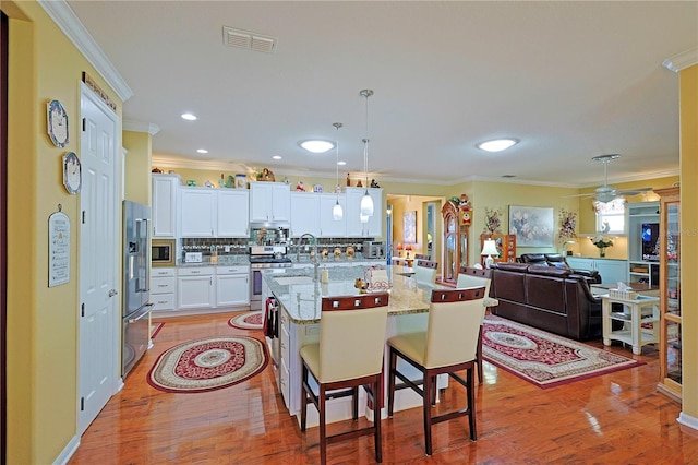 kitchen with light wood finished floors, visible vents, stainless steel appliances, and crown molding