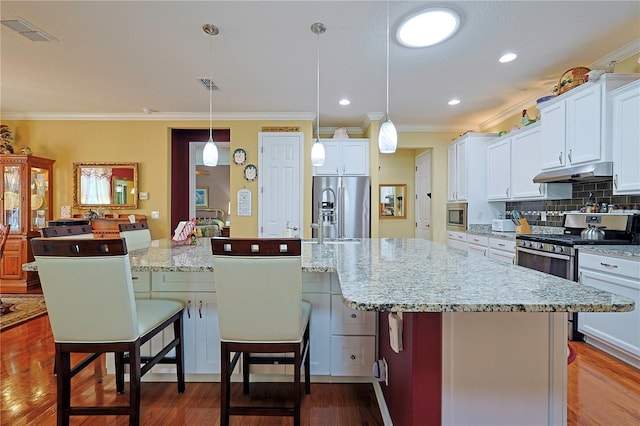 kitchen with a breakfast bar area, stainless steel appliances, tasteful backsplash, visible vents, and under cabinet range hood