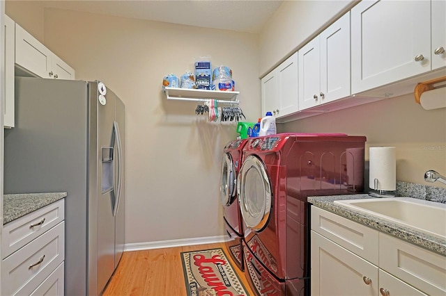 washroom featuring cabinet space, light wood-style floors, a sink, independent washer and dryer, and baseboards