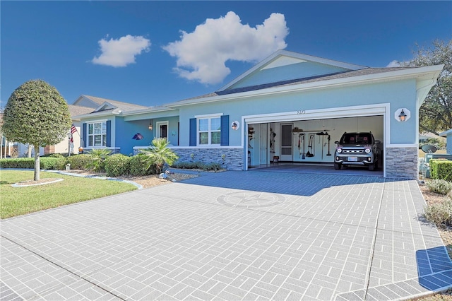 ranch-style home with a garage, stone siding, decorative driveway, and stucco siding