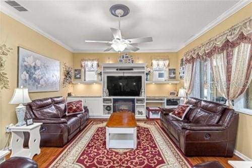 living area featuring a ceiling fan, visible vents, crown molding, and wood finished floors