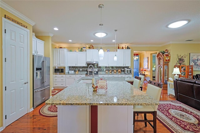 kitchen featuring wood finished floors, stainless steel appliances, a kitchen bar, white cabinetry, and a sink