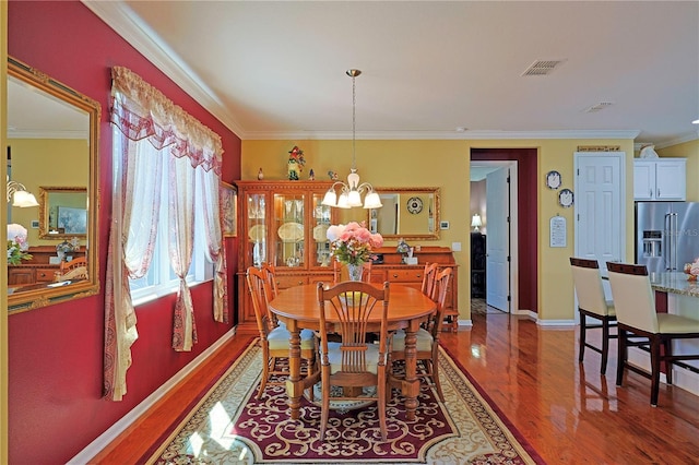 dining area featuring a chandelier, wood finished floors, visible vents, baseboards, and ornamental molding