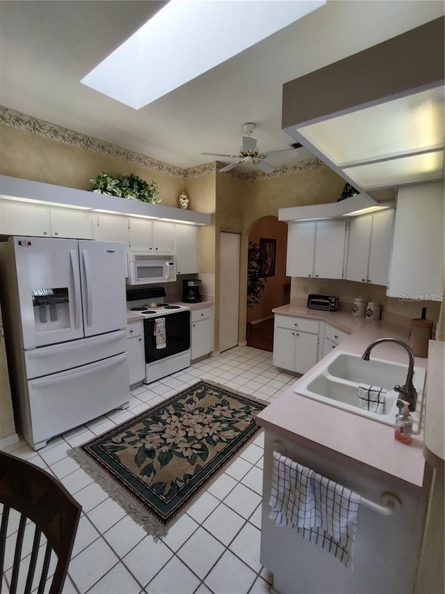 kitchen featuring white appliances, ceiling fan, light tile floors, sink, and a skylight