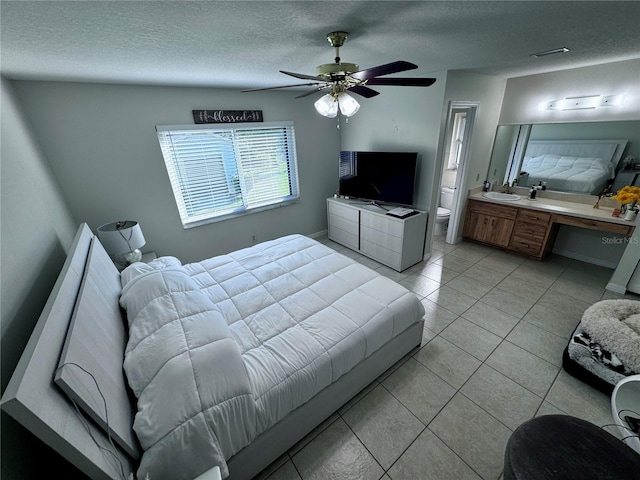 tiled bedroom with built in desk, ceiling fan, a textured ceiling, ensuite bath, and sink