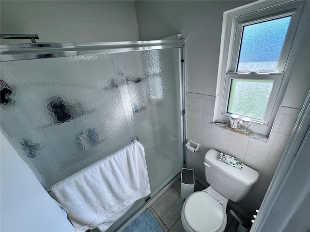 bathroom featuring a shower with door, toilet, a healthy amount of sunlight, and tile patterned floors