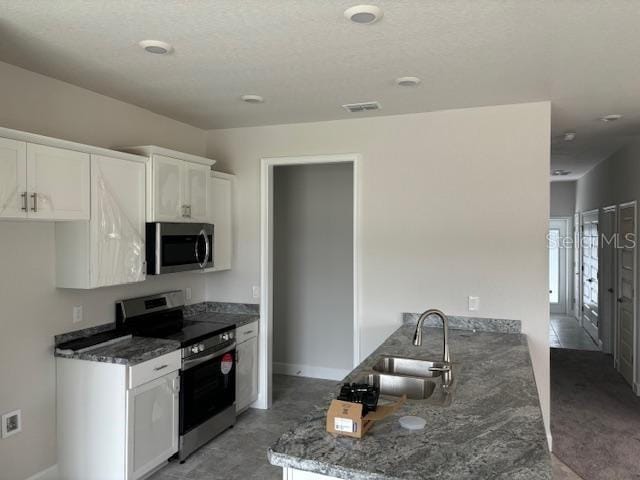 kitchen with appliances with stainless steel finishes, sink, dark stone countertops, white cabinets, and concrete floors