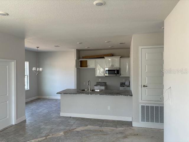 kitchen with pendant lighting, white cabinetry, dark stone countertops, a chandelier, and a textured ceiling