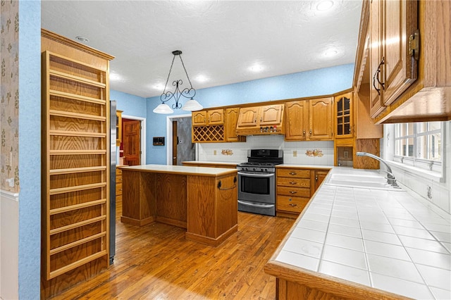 kitchen with backsplash, gas stove, sink, hardwood / wood-style flooring, and a center island