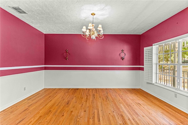 empty room featuring wood-type flooring, a textured ceiling, and an inviting chandelier