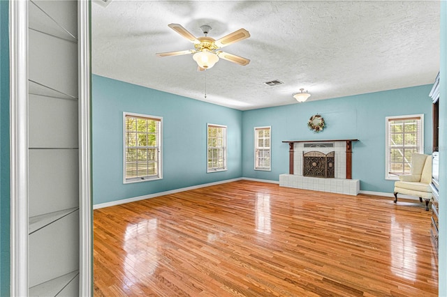 unfurnished living room with ceiling fan, hardwood / wood-style floors, a textured ceiling, and a brick fireplace