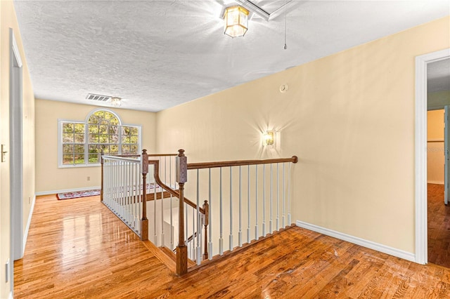 corridor with a textured ceiling and light hardwood / wood-style flooring