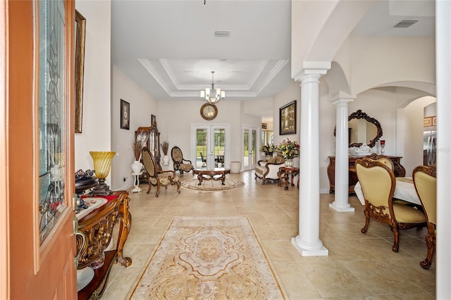 entryway featuring a tray ceiling, light tile floors, ornate columns, and an inviting chandelier