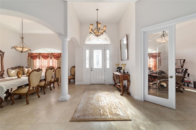 entryway featuring decorative columns, light tile flooring, a chandelier, and a towering ceiling