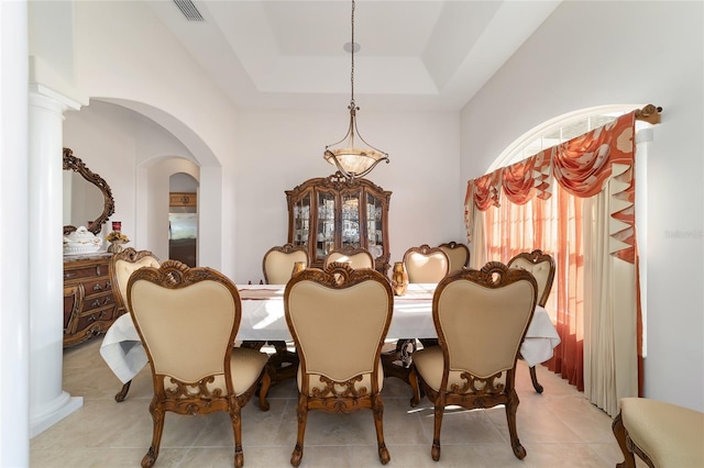 tiled dining room with a tray ceiling and ornate columns