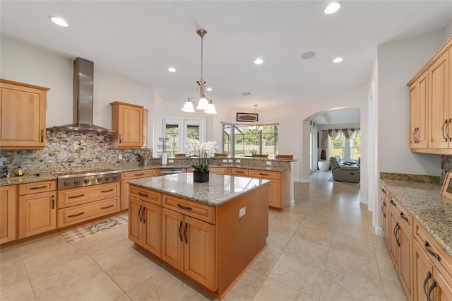 kitchen featuring decorative light fixtures, a center island, an inviting chandelier, wall chimney exhaust hood, and light stone counters