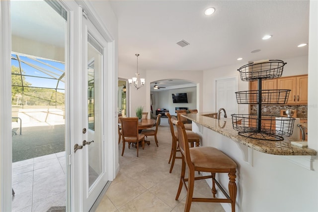 kitchen with pendant lighting, light tile floors, light stone counters, a breakfast bar area, and a notable chandelier