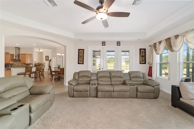 living room featuring crown molding, light colored carpet, a tray ceiling, and ceiling fan with notable chandelier