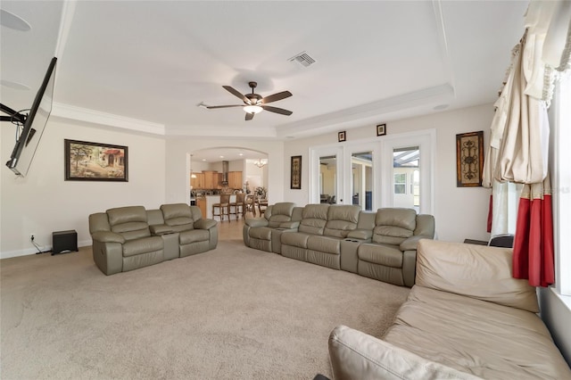 living room featuring a raised ceiling, ornamental molding, ceiling fan, and light colored carpet