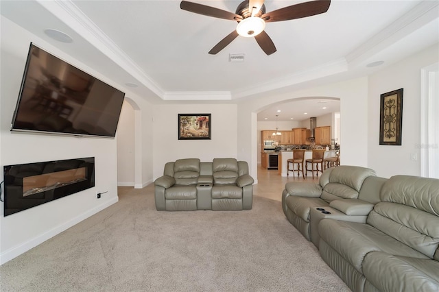 carpeted living room featuring a raised ceiling, crown molding, and ceiling fan